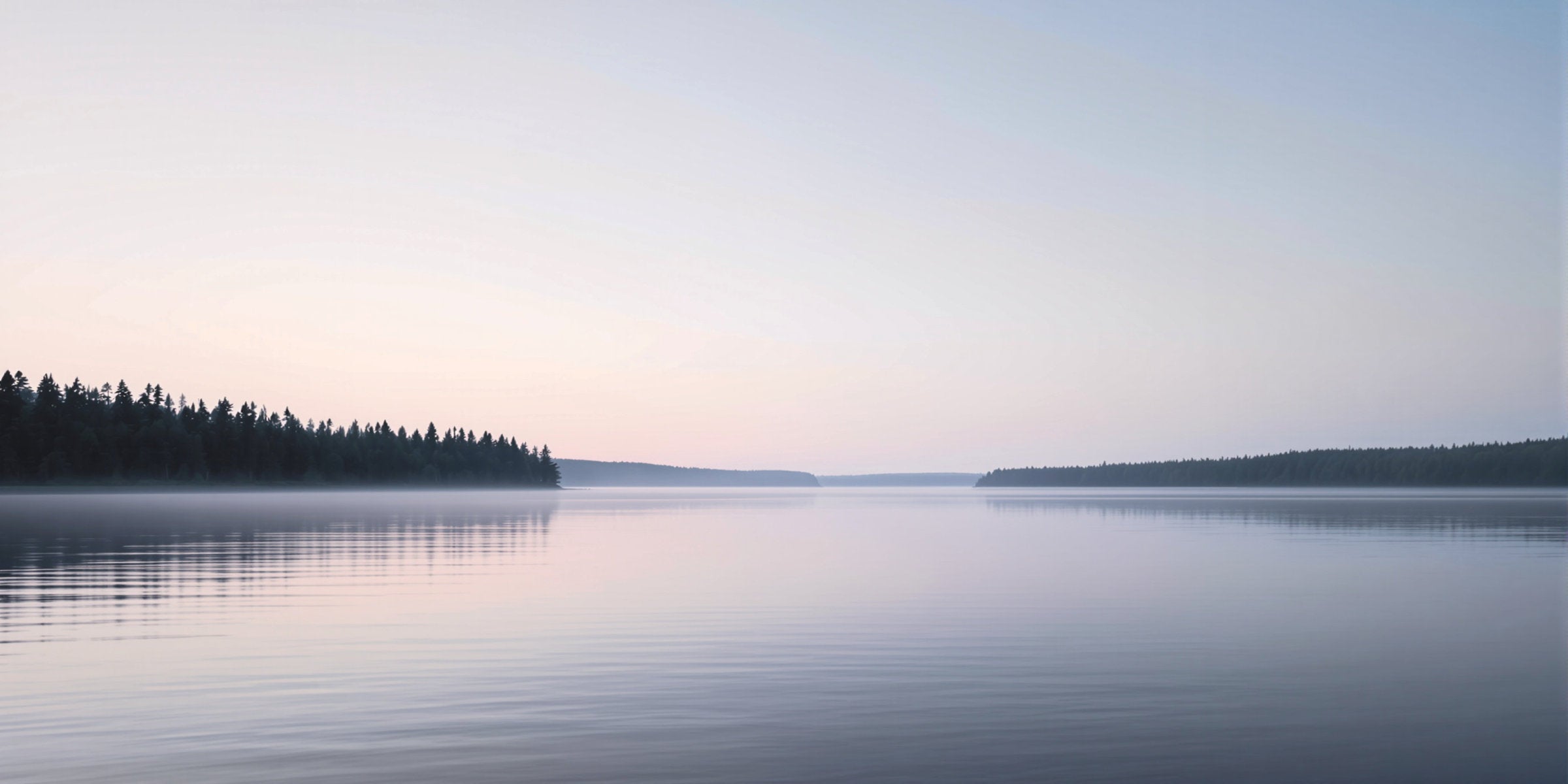 Calm Nordic lake at dusk with misty water, forest shorelines and soft pastel sky, Finland