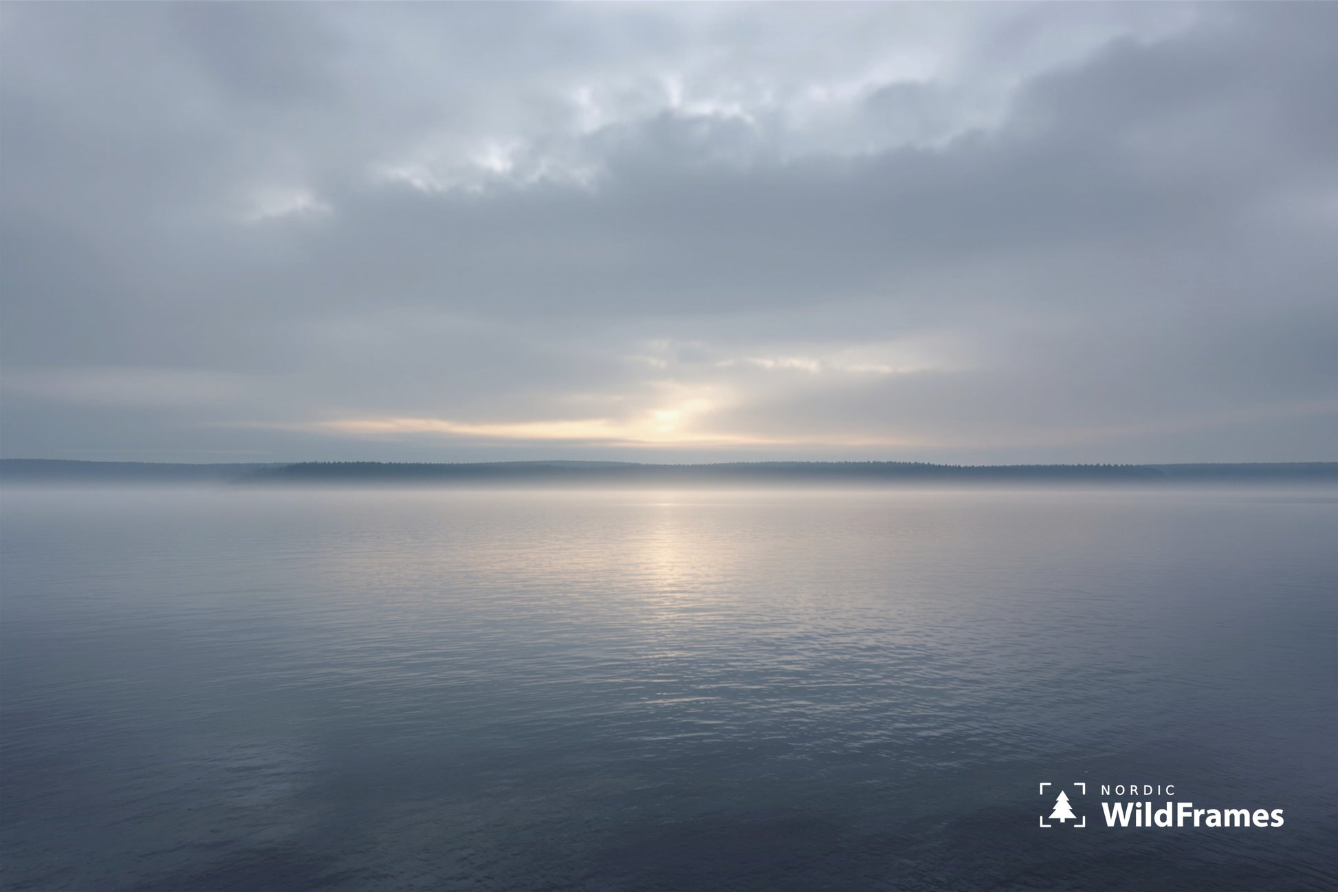 Minimal calm lake with sunlight breaking through clouds above a misty forest horizon, Finland
