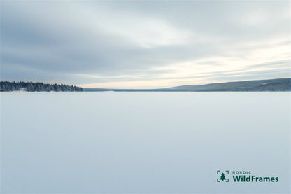 Minimal snow-covered lake expanse with distant treeline and pale winter sunset on the horizon, Finland